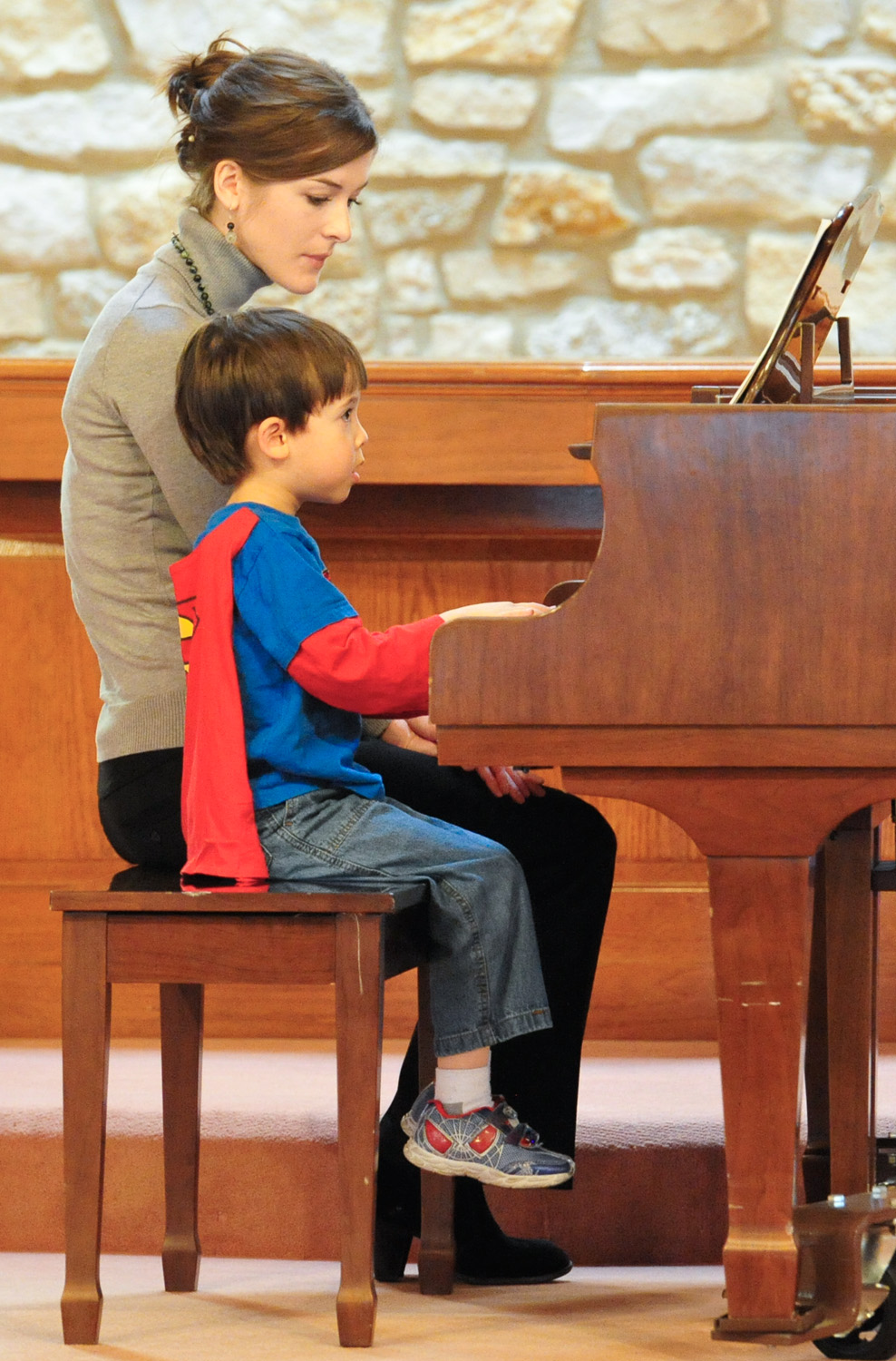 A young student in a Superman cape playing piano with his teacher at the first Cincinnati School of Music recital